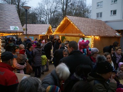 Menschenmenge auf einem festlich beleuchteten Adventsmarkt mit Holzhütten und Lichterketten