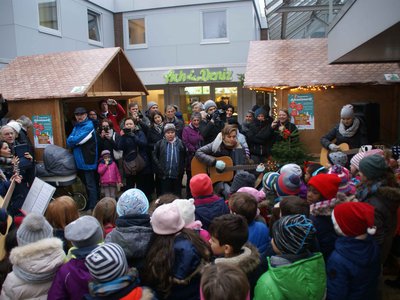 Kinder und Erwachsene vor weihnachtlich geschmückten Holzbuden auf dem Adventsmarkt