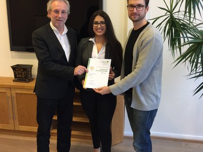 Offizielle Übergabe eines Vertragsdokuments an neue Mitarbeiterin durch zwei Mitarbeiter im Büro